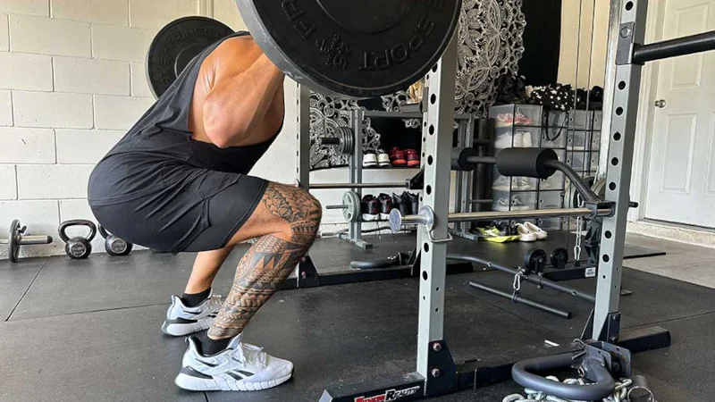 A person squats with a barbell in a garage gym